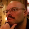 A bald man with glasses and a mustache in a restaurant.