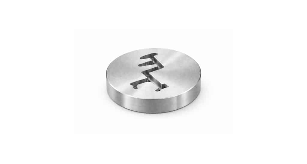 A round metal object with a precisely cut zigzag slot in the middle, made using wire EDM machining, photographed on a plain white background.