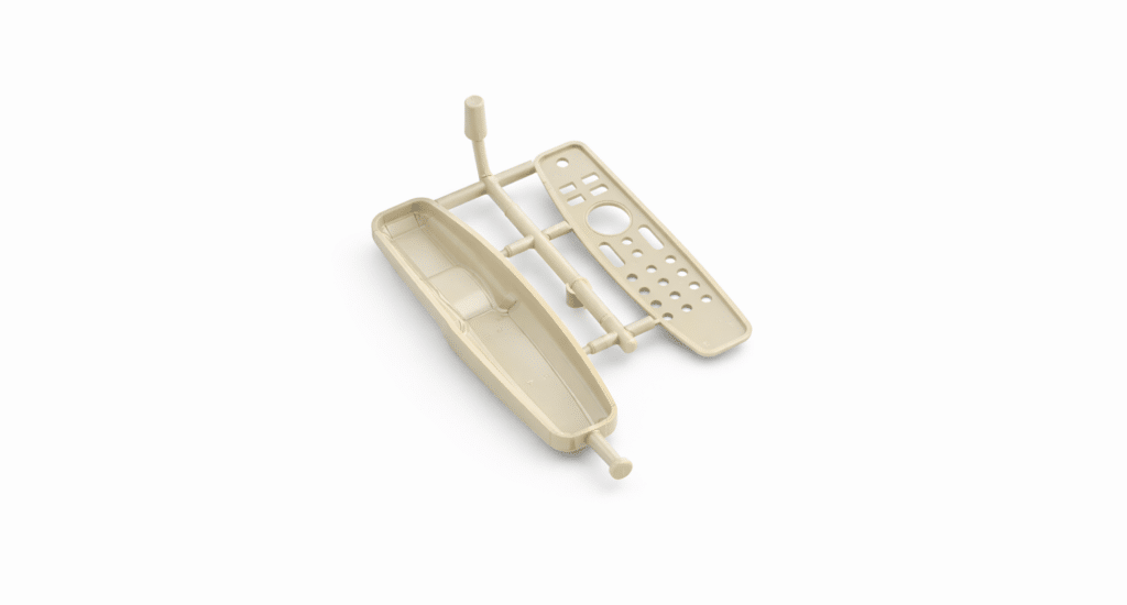 Beige plastic model kit parts resembling a small boat and a rectangular panel, connected by sprues, on a white background—an example that sparks comparison of compression molding vs injection molding techniques.