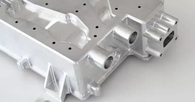 Close-up of a machined aluminum component with multiple holes, precise edges, and cylindrical protrusions, likely used in industrial or mechanical applications.