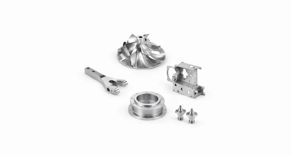 Five precision-machined metal components, including a turbine wheel, rod, flange, bracket, and two small nozzles, showcase the quality you’d expect from top precision manufacturing solutions companies on a white background.